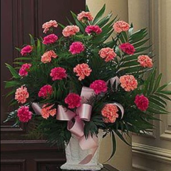 Pink and coral carnations in a white vase with a pink ribbon