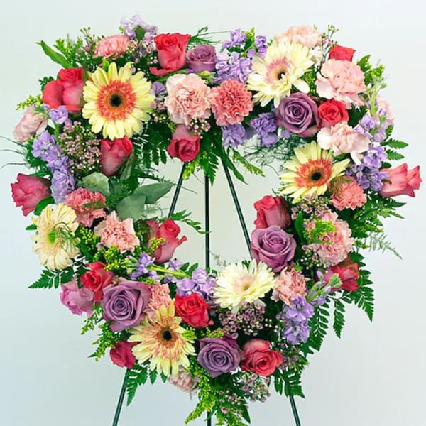 Heart-shaped floral wreath on a stand with pink, purple, and yellow blooms