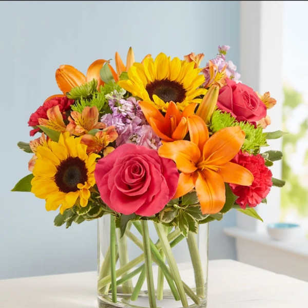 Bright mixed bouquet with sunflowers, roses, lilies, and carnations in a clear glass vase