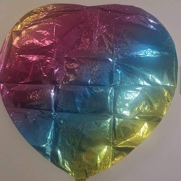 Deflated iridescent heart-shaped foil balloon with pink, blue, and yellow gradient.