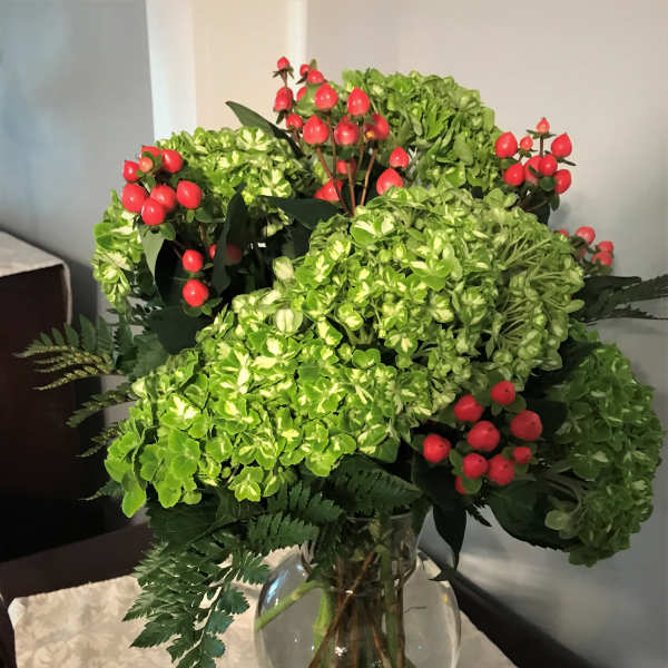 Green hydrangea bouquet with red berry stems in a glass vase