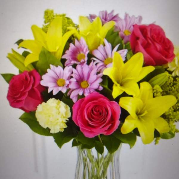 Bouquet of pink roses, yellow lilies, and lavender daisies in a clear vase