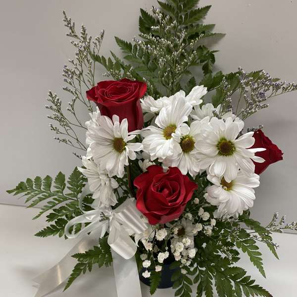 Red roses and white daisies in a vase with a white ribbon