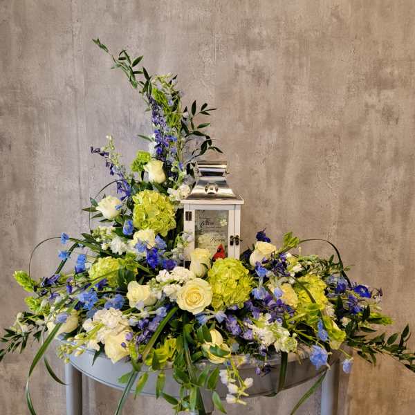 Large floral arrangement with white roses, green hydrangeas, and blue flowers around a lantern
