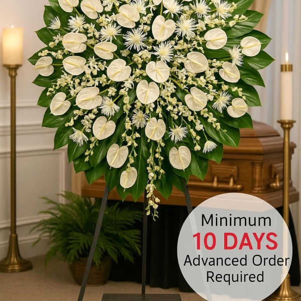 Large white standing funeral spray with heart-shaped blooms and dark green leaves on an easel before a casket