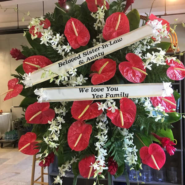 Standing sympathy spray with red tropical flowers, white orchids, and message ribbons on an easel