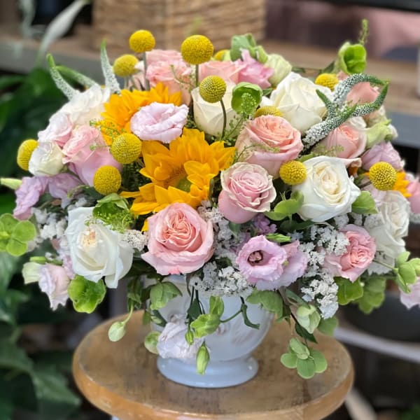 Rounded arrangement of pink and white roses with yellow sunflowers in a white ceramic vase