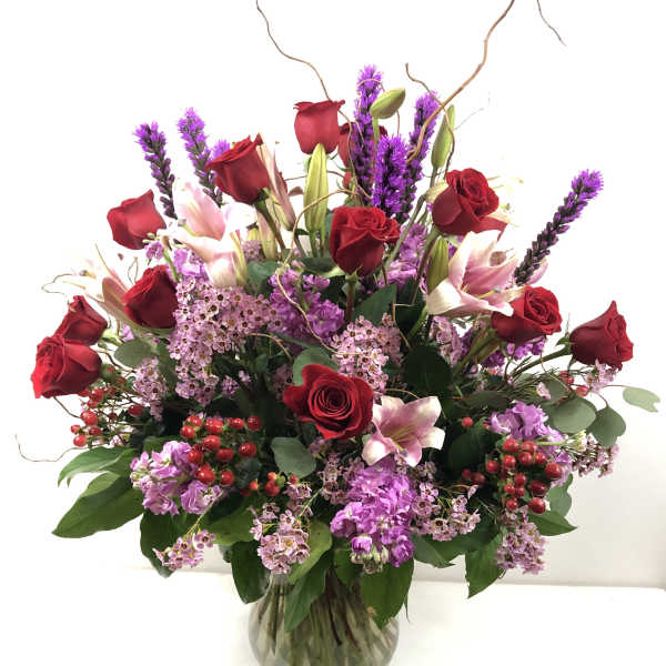 Red roses and pink lilies in a glass vase with purple filler flowers