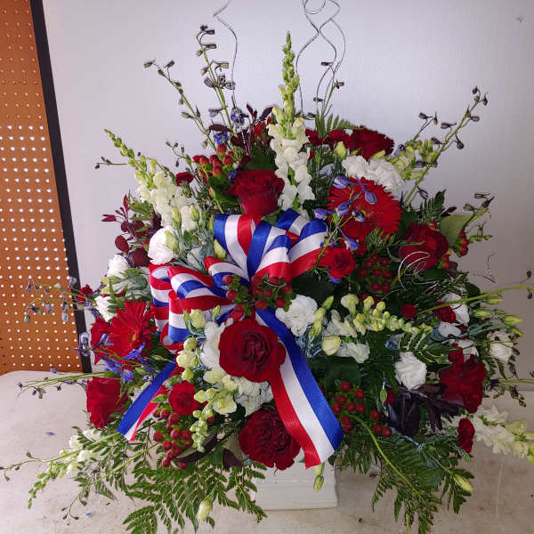 Large red, white, and blue floral arrangement with ribbon in a white container