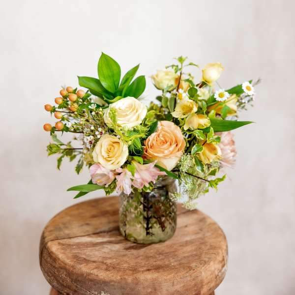 Cream and peach roses in a glass vase with small white flowers