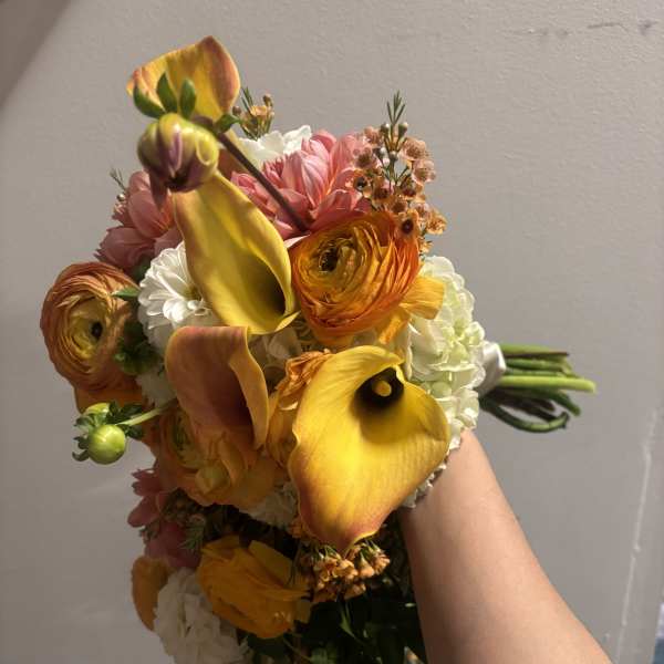 Handheld bouquet with yellow calla lilies, orange ranunculus, and pink blooms