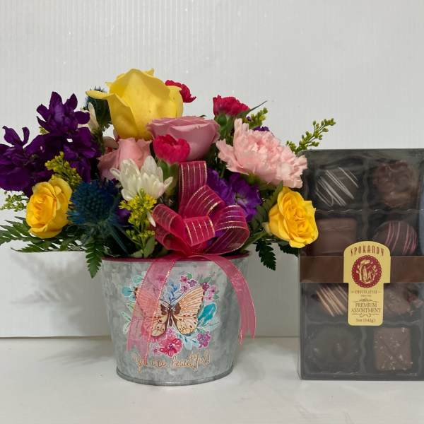 Mixed bouquet in a metal bucket beside a box of chocolates