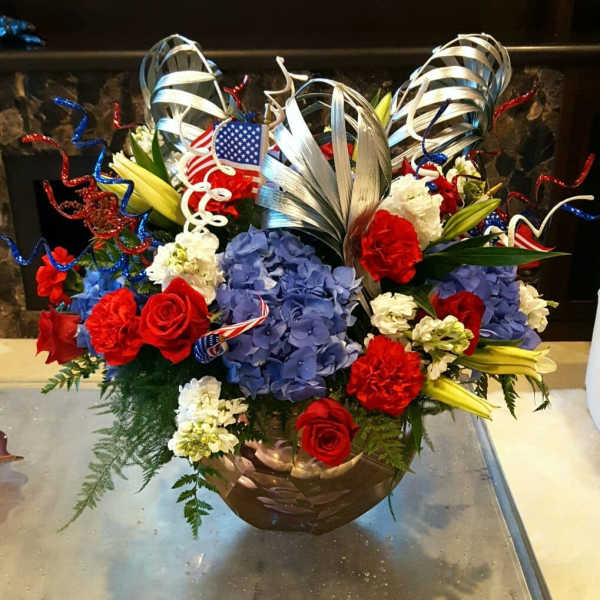 Red roses and blue hydrangeas in a bronze bowl with patriotic ribbon curls