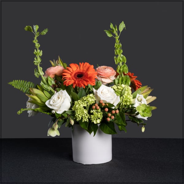Mixed floral arrangement in a white vase with orange and white blooms