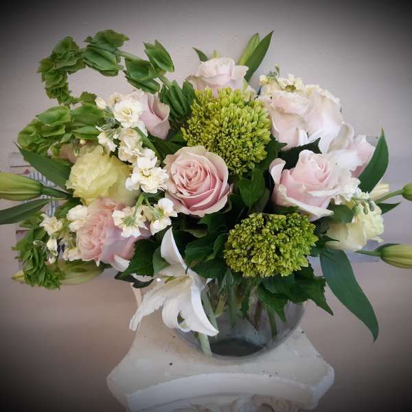 Pink and white roses arranged in a glass vase with green blooms
