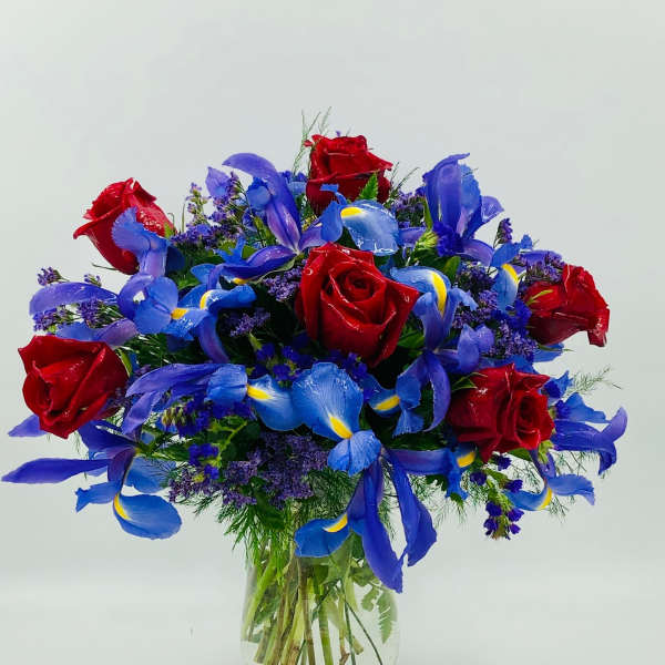Arrangement of red roses and blue irises with purple filler flowers in a clear glass vase