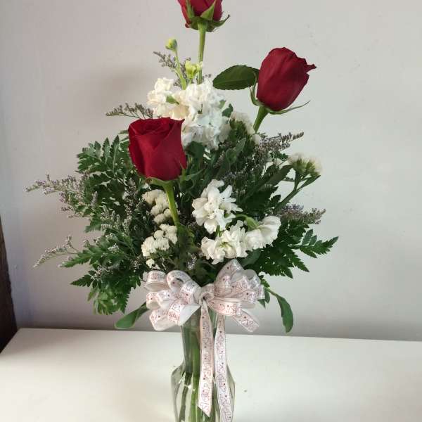Red roses and white flowers in a clear glass vase with a ribbon bow