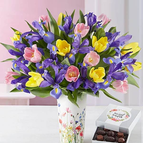 Bouquet of purple, pink, and yellow tulips in a floral vase beside a box of chocolates