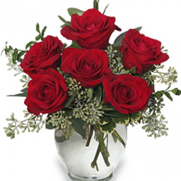 Red roses arranged in a clear glass vase with greenery