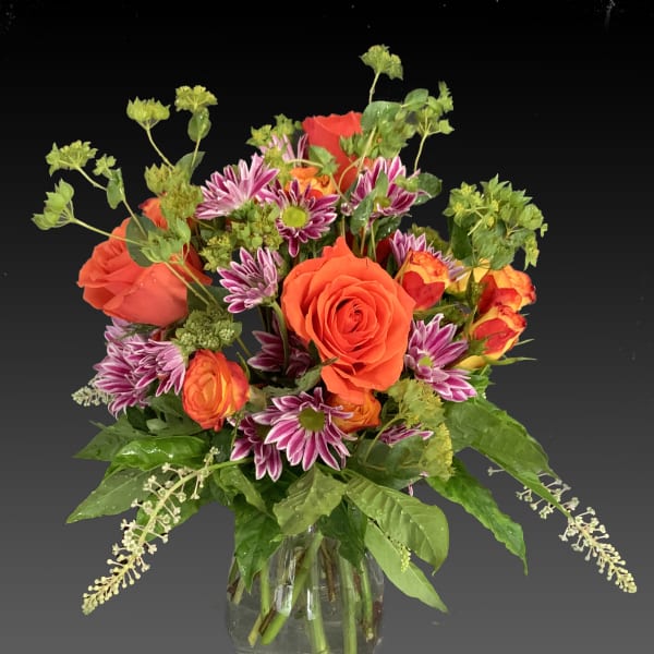 Bouquet of orange roses and purple daisies in a clear glass vase
