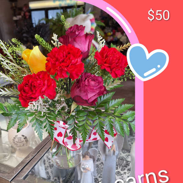 Mixed bouquet of roses and carnations in a glass vase with a heart ribbon.