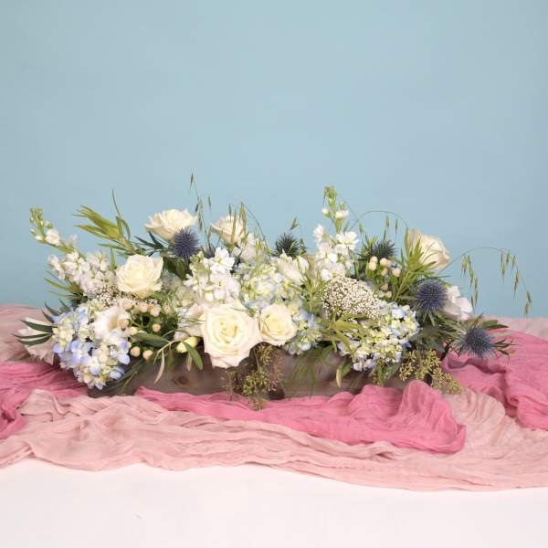 Low floral centerpiece with white roses and blue accents on pink fabric