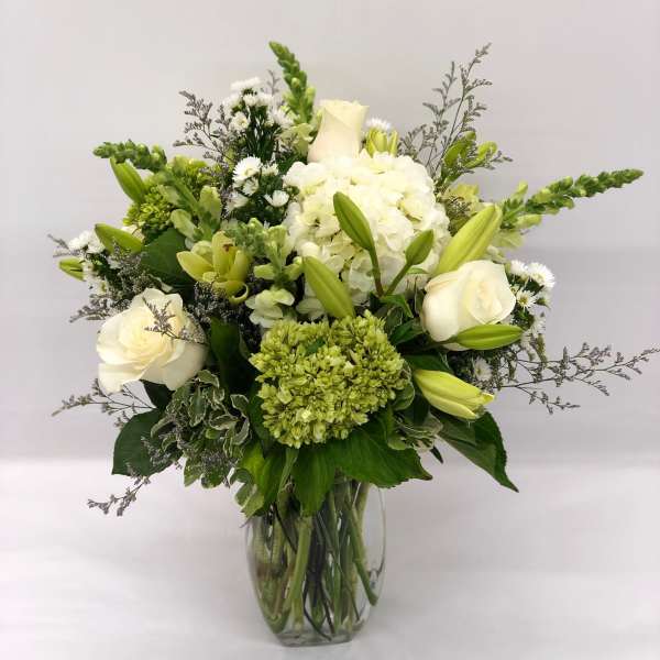 Tall arrangement of white and green roses, lilies, hydrangeas, and snapdragons in a clear glass vase.