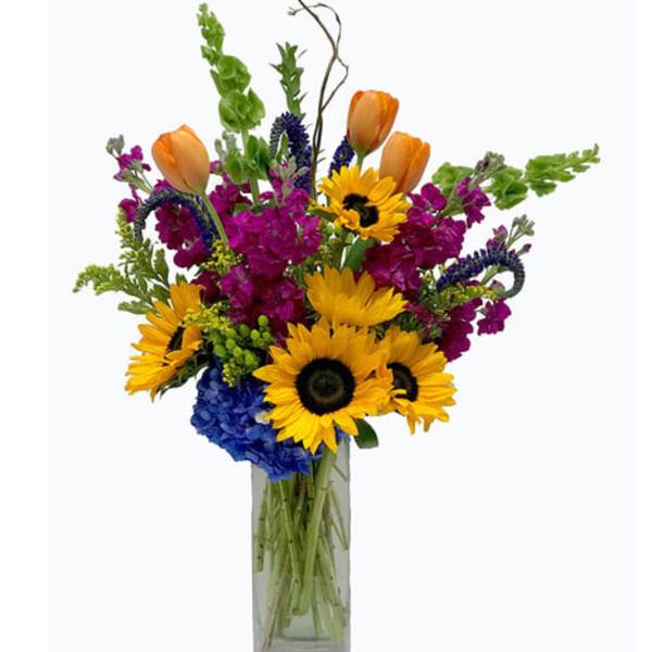 Mixed bouquet with sunflowers, orange tulips, and purple blooms in a glass vase