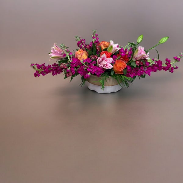 Low floral centerpiece with pink, orange, and magenta blooms in a white bowl vase