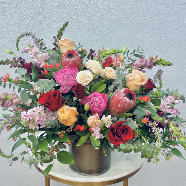 Mixed bouquet of roses, protea, and pink blooms in a metal vase