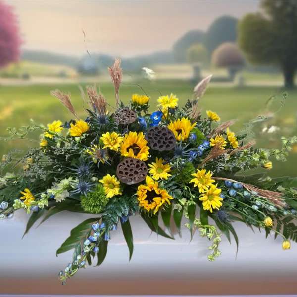 Yellow and blue floral casket spray with greenery and dried accents