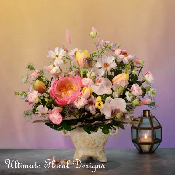 Pink and white mixed flower arrangement in a cream vase beside a lantern