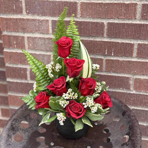 Red roses arranged in a black vase with greenery and white filler flowers