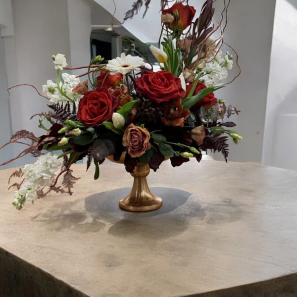 Red rose arrangement in a gold pedestal vase with white blooms