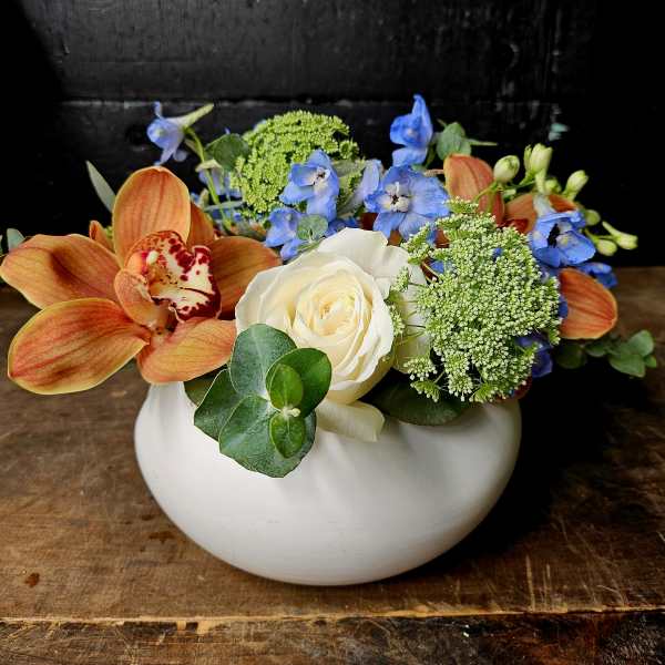 Orange orchids and a white rose in a white bowl vase