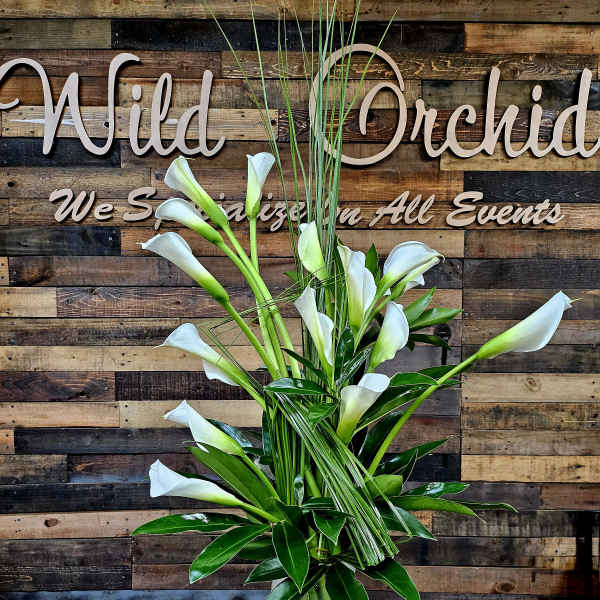 White calla lilies in a clear glass vase with tall grass accents