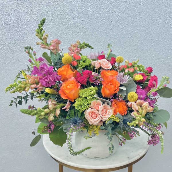Mixed bouquet of orange, pink, and purple flowers in a white vase
