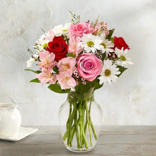 Bouquet of pink and red roses with white daisies in a clear glass vase