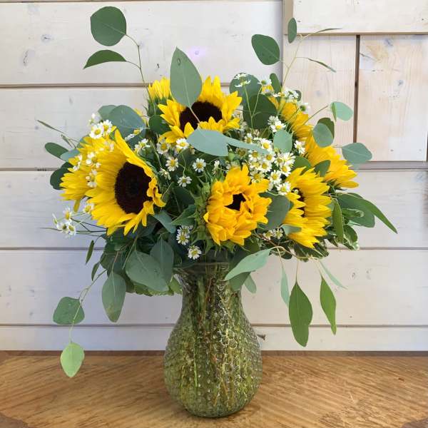 Sunflower bouquet in a textured glass vase with small white daisies