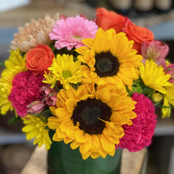 Bright mixed bouquet with sunflowers, roses, gerbera and carnations in a green glass vase