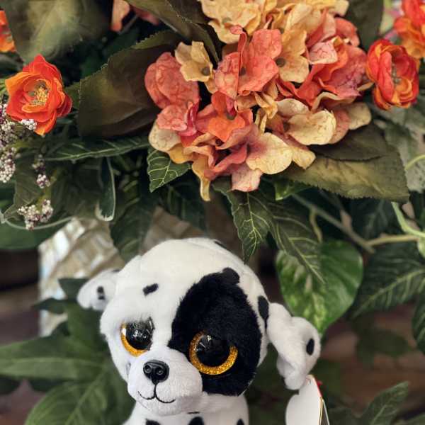 Plush Dalmatian puppy in front of an orange and peach floral arrangement
