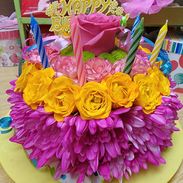 Bright pink and yellow floral birthday cake with candles and ribbon