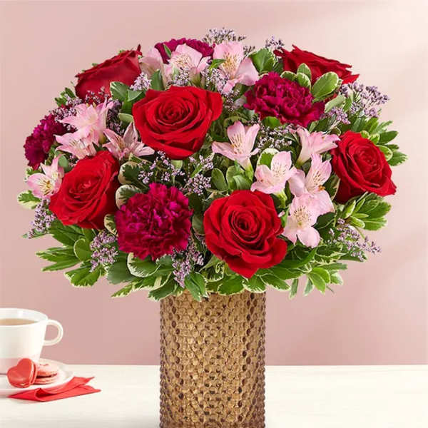 Red roses and pink flowers arranged in a textured vase