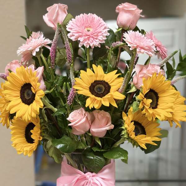 Bouquet of pink roses and yellow sunflowers in a clear vase with a pink ribbon