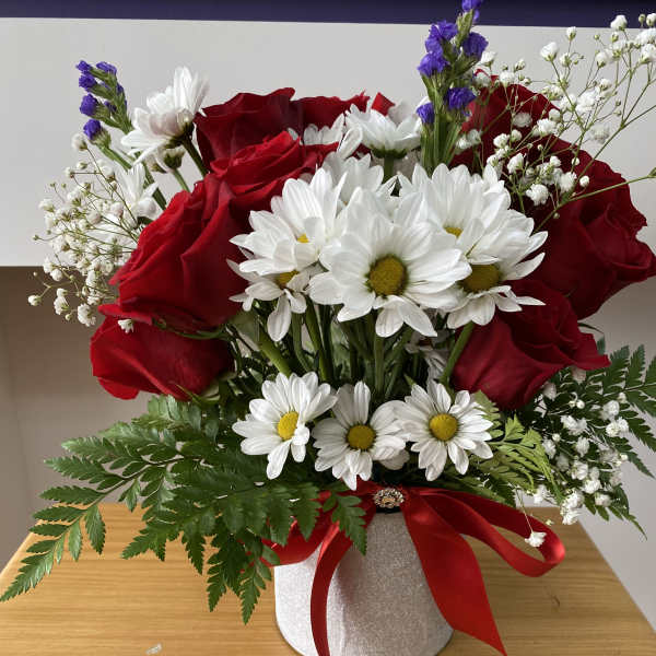 Red roses and white daisies arranged in a glittery hatbox with a red ribbon