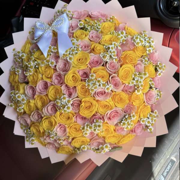Round bouquet of pink and yellow roses with small white daisies and a blue bow
