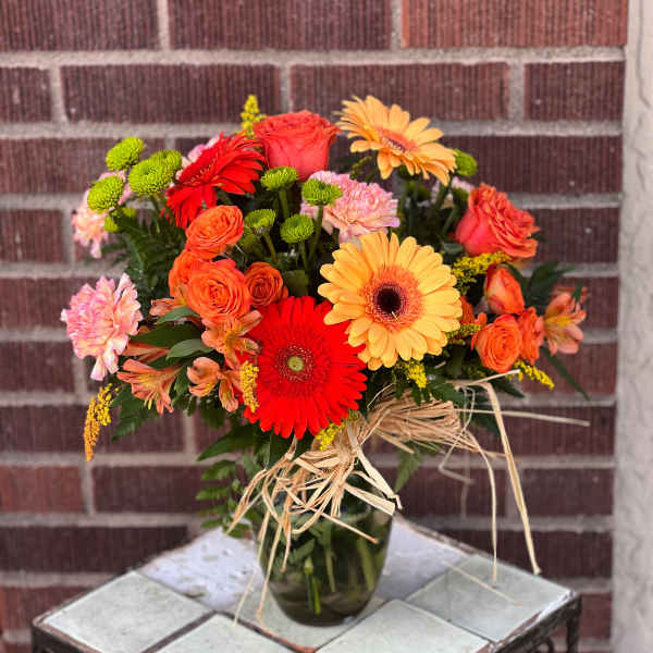 Mixed bouquet of orange, red, and pink flowers in a glass vase