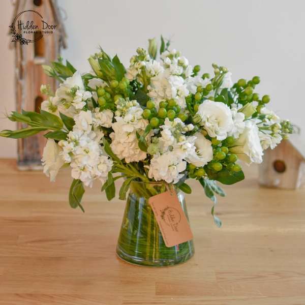 White floral arrangement in a glass vase with green berries