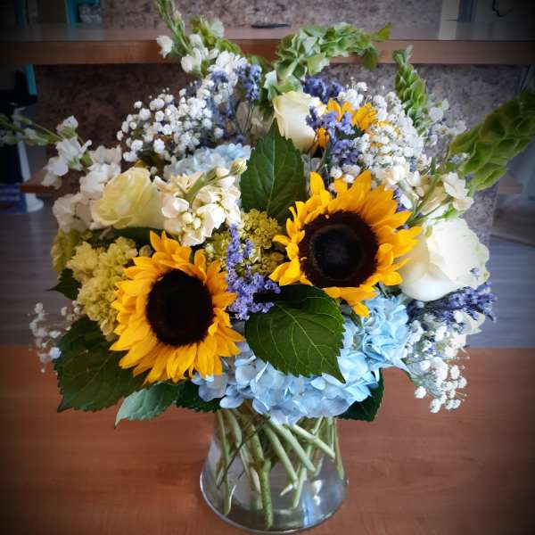 Sunflowers, blue hydrangeas, and white roses in a glass vase