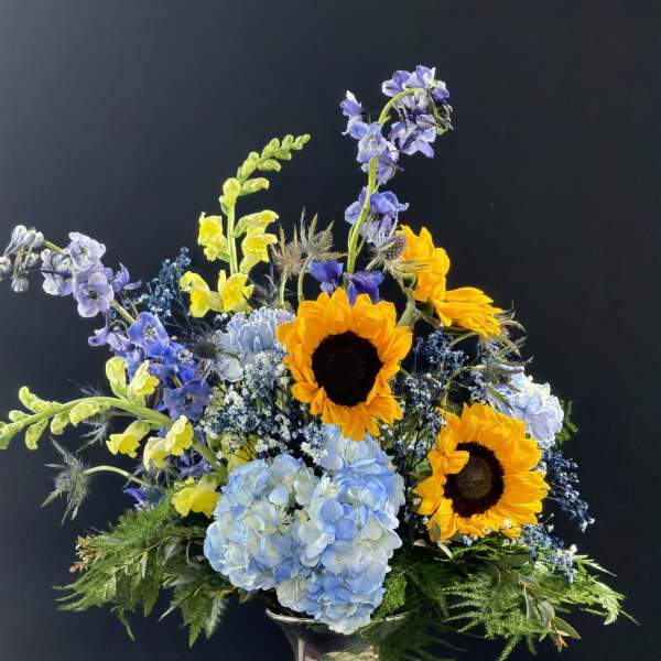 Mixed bouquet with sunflowers, blue hydrangea, and purple flowers in a silver vase